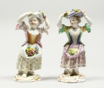 TWO SMALL MEISSEN PORCELAIN FIGURES OF YOUNG GIRLS holding a bundle above their head , with