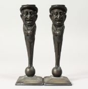 A PAIR OF JUDAICA BRONZE CANDLESTICKS of men, the hat as a candle holder, the man standing on a