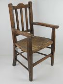 A vintage oak child's straw seated open armchair.