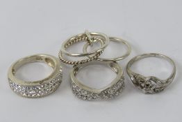 Four silver rings sizes I-K, each stamped 925, one being small floral ring set with diamonds.