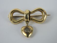 A yellow metal brooch in the form of a bow having heart suspended below, 2.8cm wide, 2.