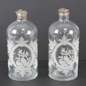 Two 'apothecary' style glass bottles having etched floral design to front, each with stopper,