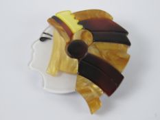 An overlaid plastic brooch in the style of Lea Stein in the form of a Native American, 4.5cm wide.