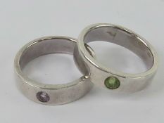 A pair of rings each stamped 925, one with lime green stone, the other with purple stone,