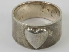 An Arts and Crafts style silver ring having central raised heart motif, graduated band 1.
