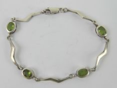 A silver and peridot bracelet having four oval cut stones separated by lightning bolt shaped panels,