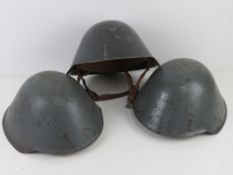 Three DDR NVA East German helmets with liners and chin straps.
