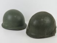 Two US helmets; one having netting attached, both with liners and chin straps.