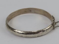 A silver hinged bangle having floral engraving, with safety chain, stamped 925.