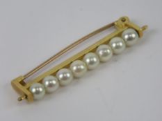 A yellow metal brooch set with eight pearls on wire bar, no apparent hallmarks, 4cm in length, 3.4g.