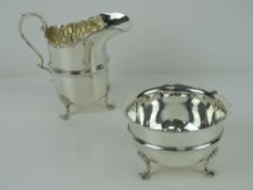 An HM silver sugar bowl and cream jug each raised over three clam shell legs,