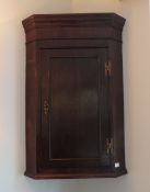 A Georgian oak hanging corner cabinet, door opening to reveal straight cut shelves within,