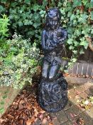 A painted stone garden figurine of a seated girl holding an oversized Lily flower.