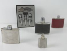 Four stainless steel hip flasks together with a bottle opener set with three stoppers. Five items.
