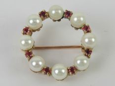 A 9ct gold wreath pendant / brooch having eight pearls alternating with eight round cut rubies,