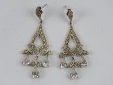 A pair of silver cocktail earrings having diamond design with white stone teardrops below,