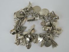 A charm bracelet profusely adorned with silver and white metal charms inc 'opera glasses' stamped