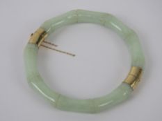 A 14ct gold and jade bangle, the pale opaque green jade carved into a bamboo pattern,
