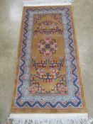 A Chinese woollen rug, gold ground with blue and pink floral design upon,