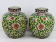 A pair of Oriental lidded ginger jars in yellow ground with green and orange floral decoration upon,