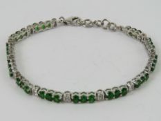 A silver tennis bracelet set with green