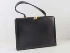 A vintage black leather handbag opening to reveal suede lining within, 30cm wide.