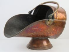 A copper coal scuttle having hinged handle over, raised over single foot, approx 45cm in length,
