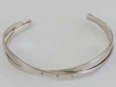 A HM silver bangle having crossover design set with three white stones, hallmarked for London, 17.