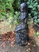 A painted stone garden figurine of a seated girl holding an oversized lily flower. In two sections.