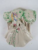 A Clarice Cliff wall pocket in the form of a lady in corseted dress before a forest,