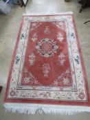 A terracotta ground woollen rug having Oriental style foliate pattern in green, purple and cream,