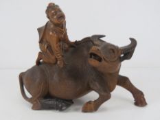 A finely carved and detailed wooden recumbent water buffalo with seated figure upon, slightly a/f,