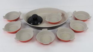 Le Cruset; a large oval oven dish together with a set of eight individual dishes and a teapot lid.