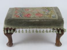 A footstool upholstered in tapestry fabric and raised over cabriole legs.