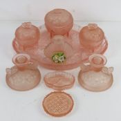 An early 20thC dressing table set in peach coloured glass comprising trays, storage pots,