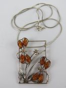 A large silver and Baltic amber pendant featuring two dragonflies over a plant, with chain necklace,