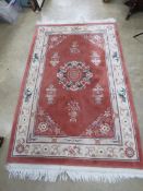 A terracotta ground woollen rug having O