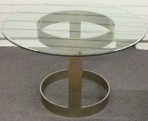 A designer circular bevelled glass dining table raised on an industrial style metal base, probably