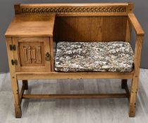 A light oak upholstered telephone seat in the Arts and Crafts style, with linen fold and adzed