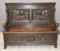 Carved oak settle with dog head arms and carved mythical creatures to back, W141 x D52 x H110cm