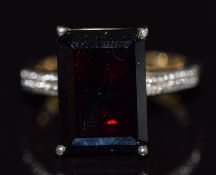 A 9k gold ring set with an emerald cut garnet and a diamond to each shoulder, 6.2g, size N