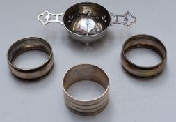 Three hallmarked silver napkin rings and a hallmarked silver tea strainer, width 11.5cm, weight 88g