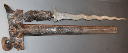 An eastern Kris dagger with 38cm blade, heavily carved handle and scabbard and glass inset gilt