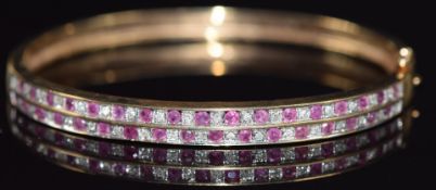 A 9ct gold bangle set with two rows of alternating rubies and diamonds, 14.4g