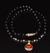 A beaded onyx necklace with a 9ct gold pendant set with a fire opal cabochon and a 9ct gold clasp