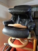 A contemporary black leather swivel adjustable armchair with matching footstool