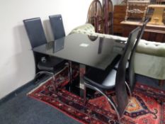 A contemporary glass pedestal dining table and four chrome and black leather chairs