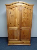 A pine shaped top double door wardrobe fitted with drawer beneath,