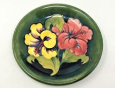 A Walter Moorcroft 'Hibiscus' pattern plate on green ground, Queen Mary Label, diameter 22cm.