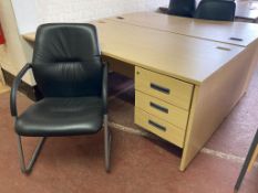 A three drawer oak effect desk, width 160 cm together with a black leather chair.